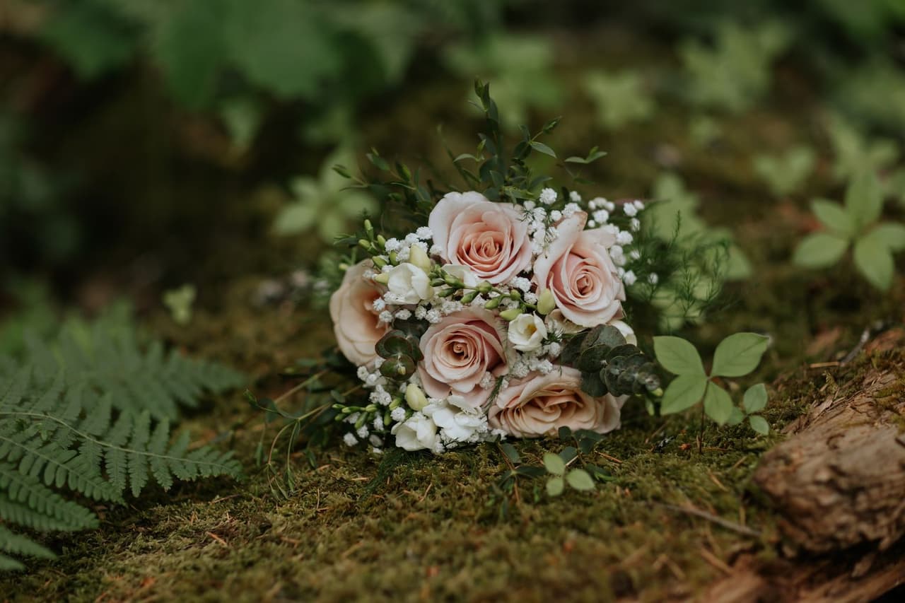 Blush roses and white baby's breath bouquet resting on moss in an intimate backyard garden setting