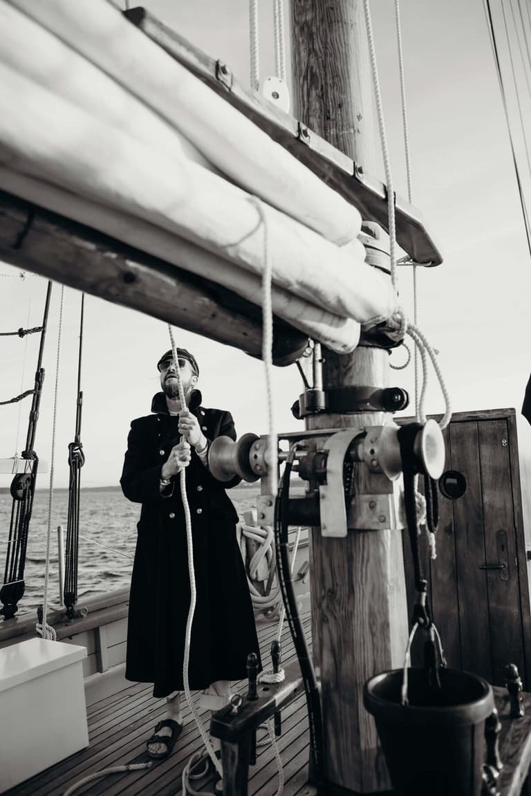 Crew member in a long coat hauling a line at the mast