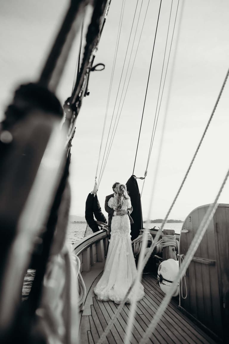 Couple embracing at the bow, framed down the rope-lined deck