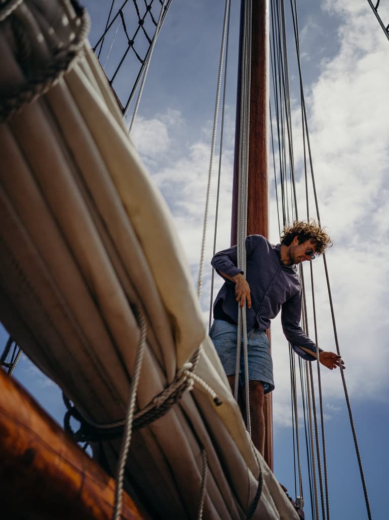 Crewman balancing aloft on the furled sail against blue sky