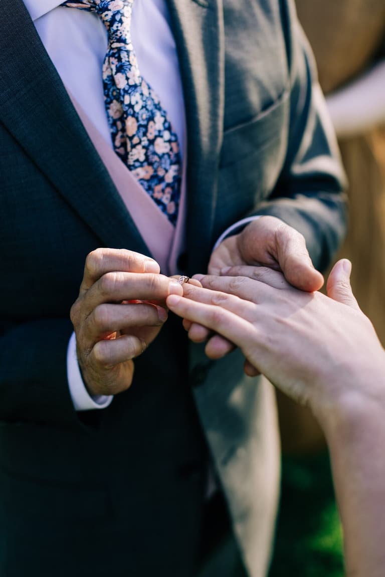 Groom in a floral tie placing a ring on the bride's hand