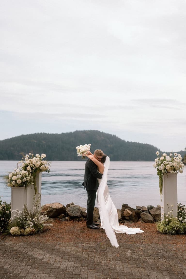 Oceanfront ceremony flowers by Crescendo Floral Studio framing an embracing couple