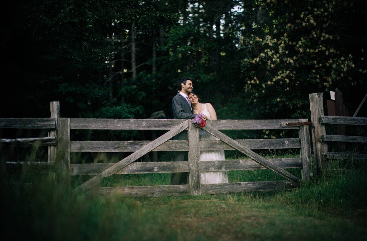 Newlyweds leaning on a weathered farm gate at dusk