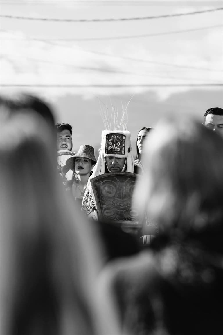 Black-and-white glimpse of a regalia dancer between watching guests