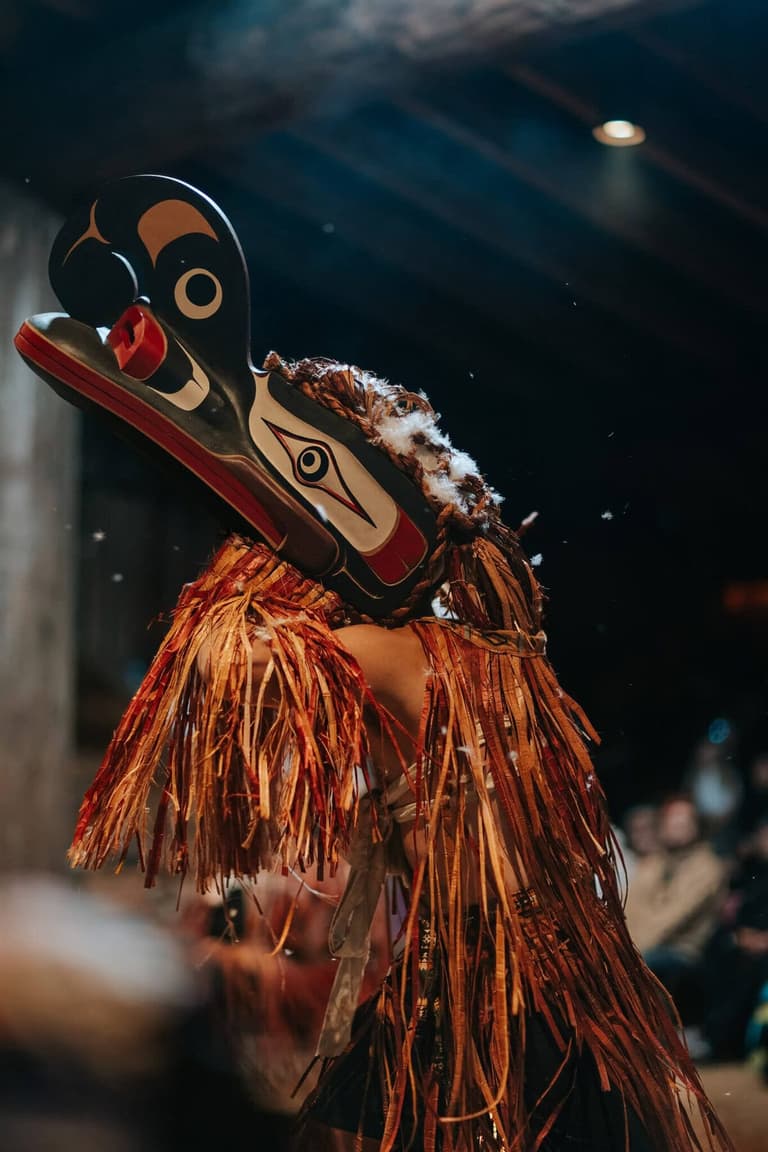 Dancer performing in a carved raven mask and cedar-bark regalia