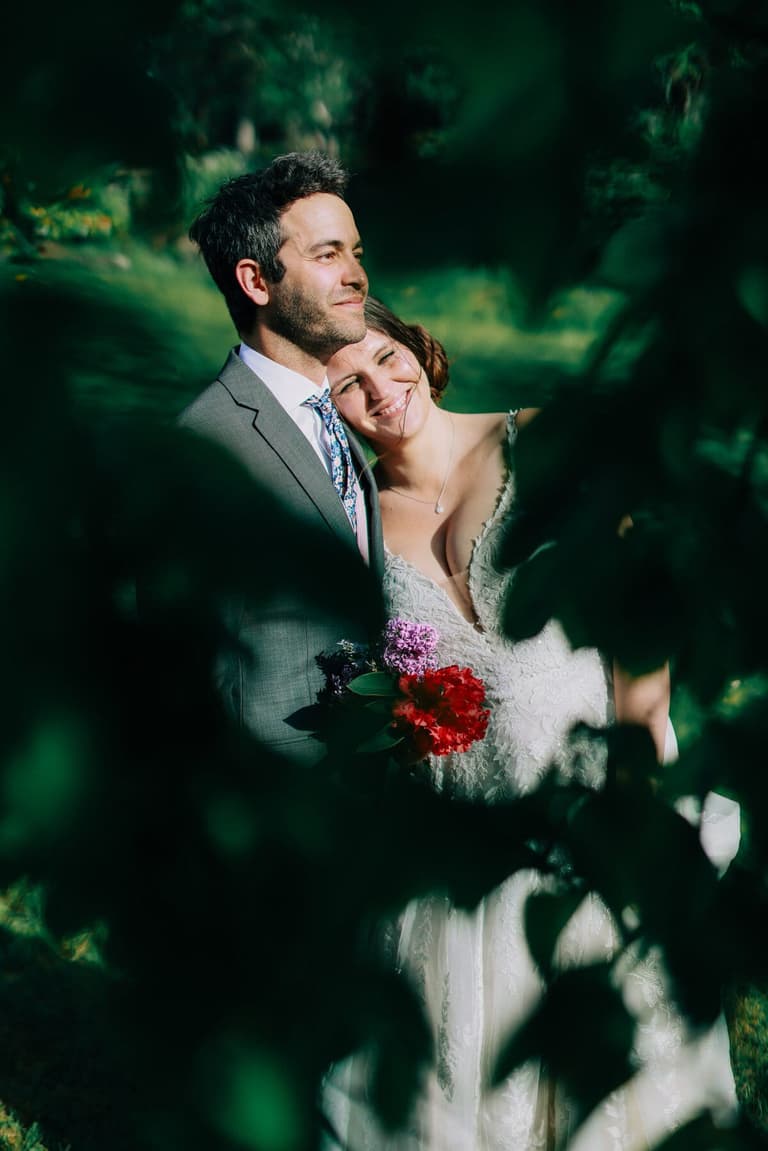 Sunlit portrait framed by leaves, bride nestled against the groom