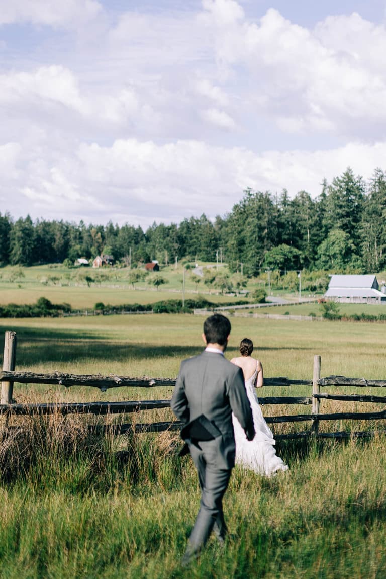 Groom following his bride through tall grass along the fence