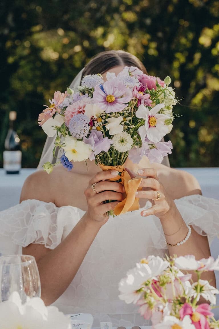 Bride peeking from behind a pastel cosmos bouquet by Gossip Floral