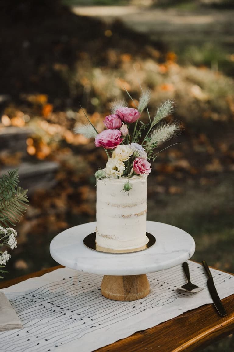 Single-tier buttercream wedding cake crowned with pink blooms and grasses