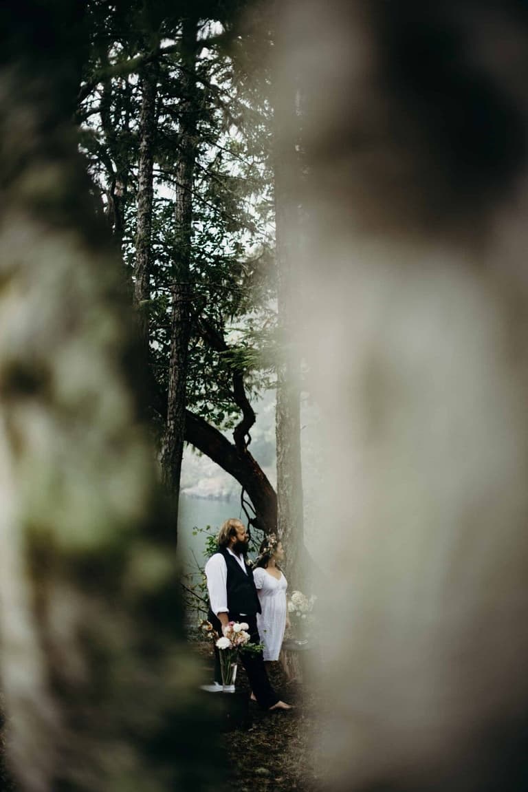 Bride and groom glimpsed through mossy trees at the water's edge