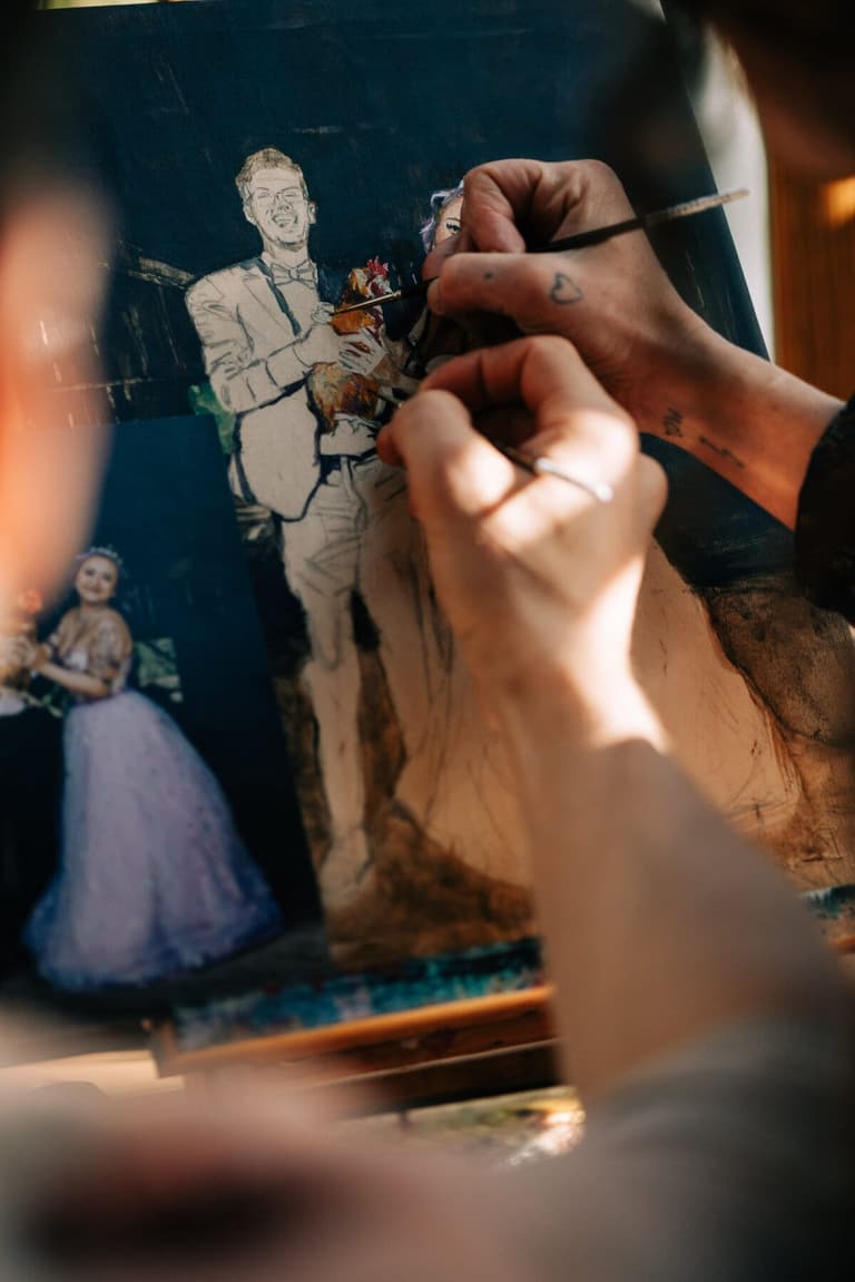 Two artists' hands painting the groom on a live wedding canvas