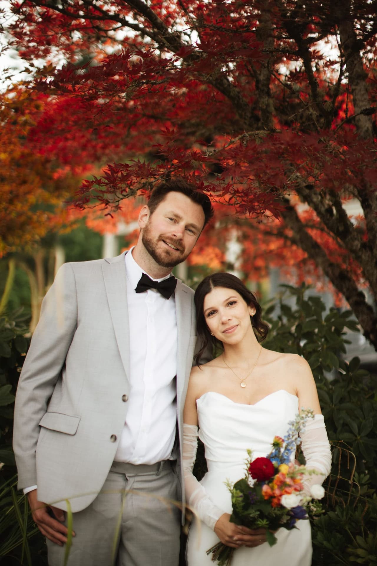 Bride and groom embrace beneath crimson autumn leaves at Church and State Winery