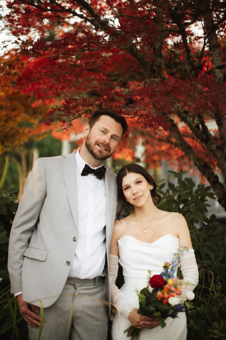 Bride and groom embrace beneath crimson autumn leaves at Church and State Winery