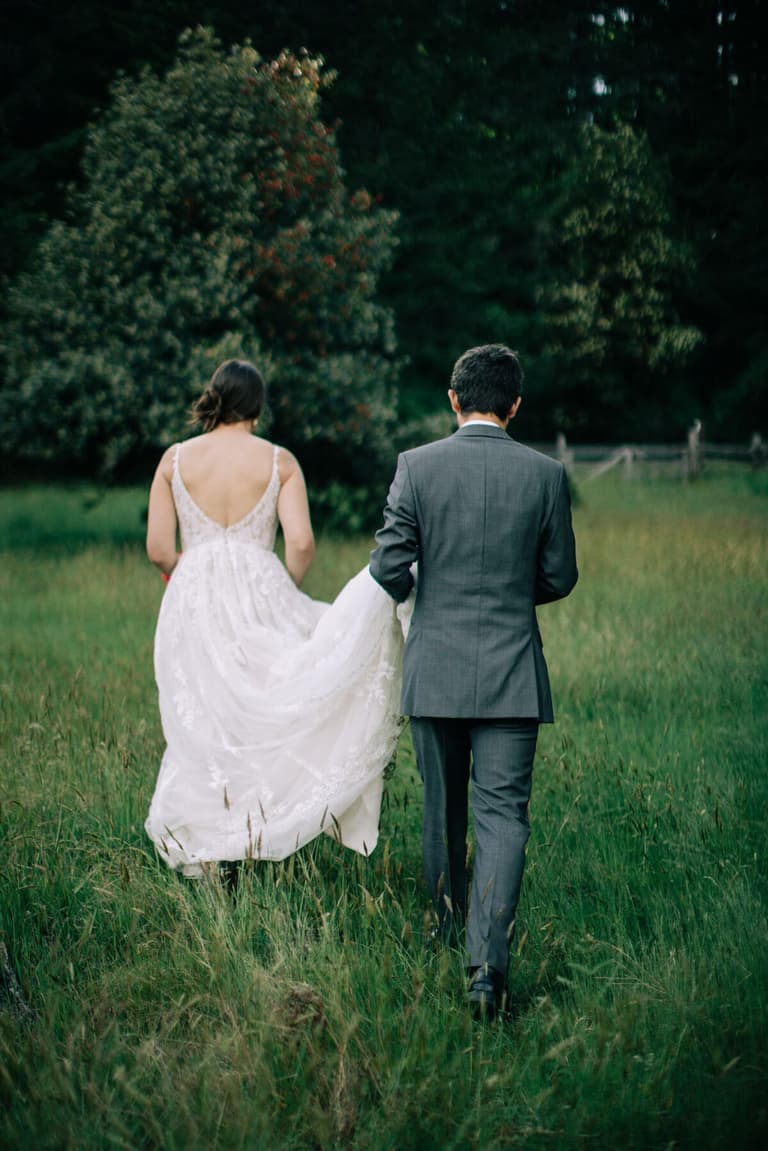 Groom carrying the lace train as they cross the field