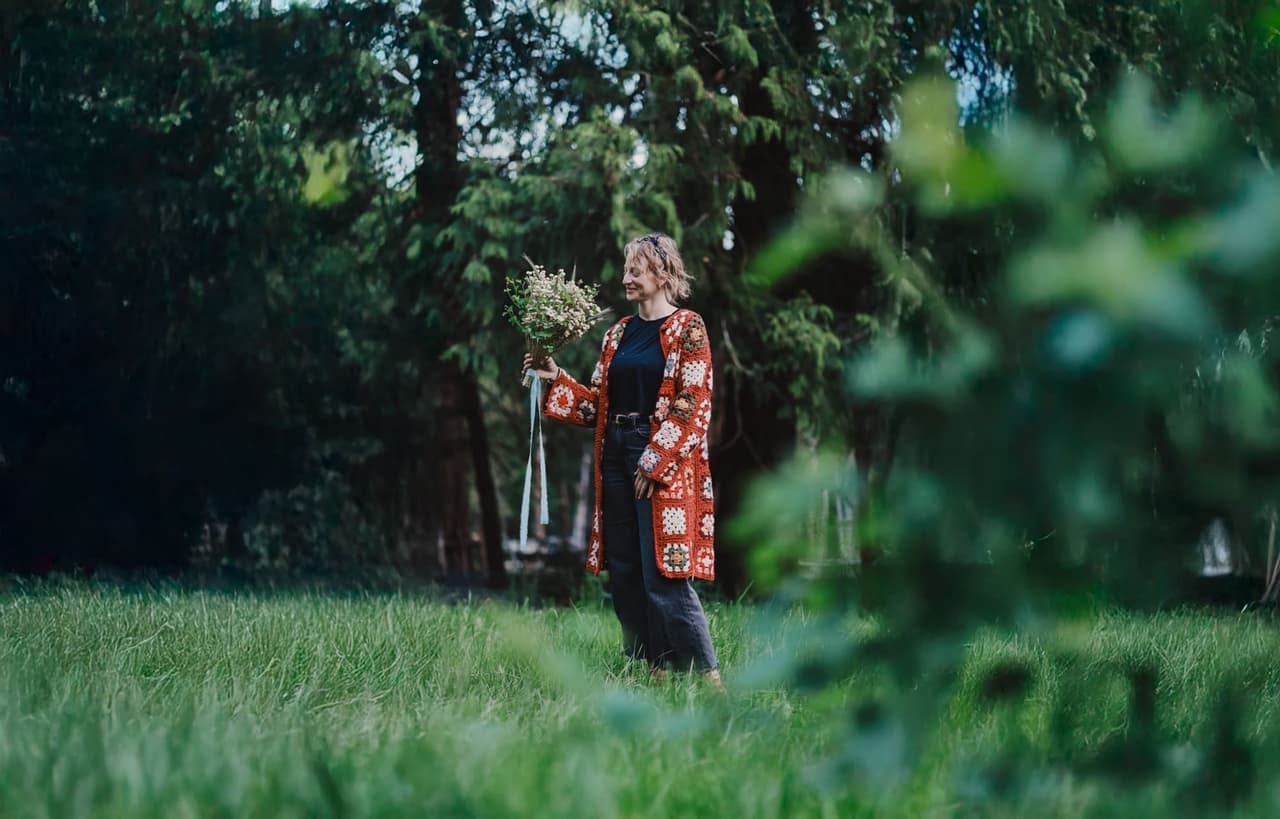 Woman holding white wildflower bouquet stands in garden beneath evergreen trees on Salt Spring Island