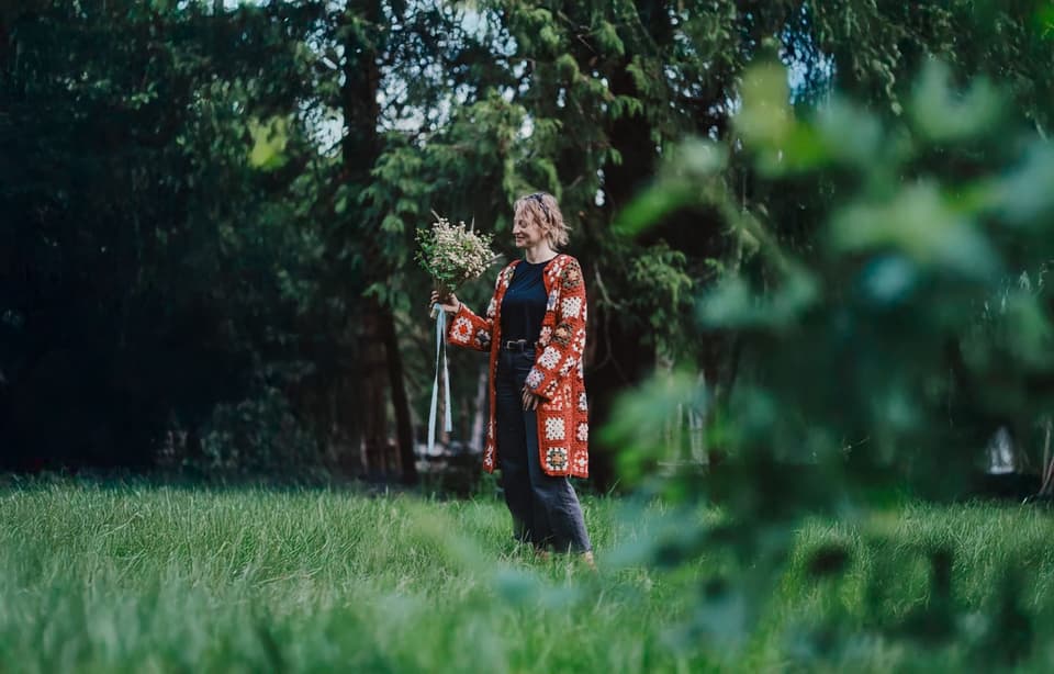 Woman holding white wildflower bouquet stands in garden beneath evergreen trees on Salt Spring Island