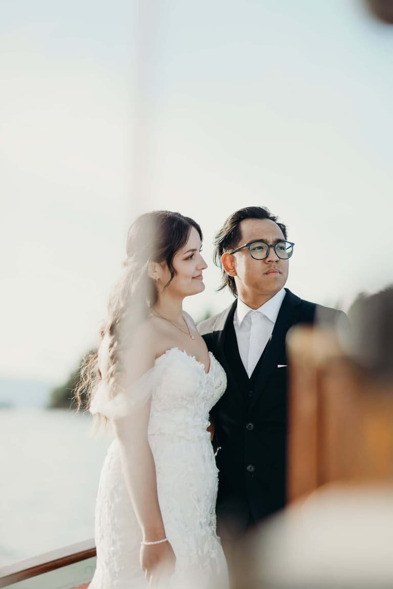 Bride and bespectacled groom gazing seaward from the rail