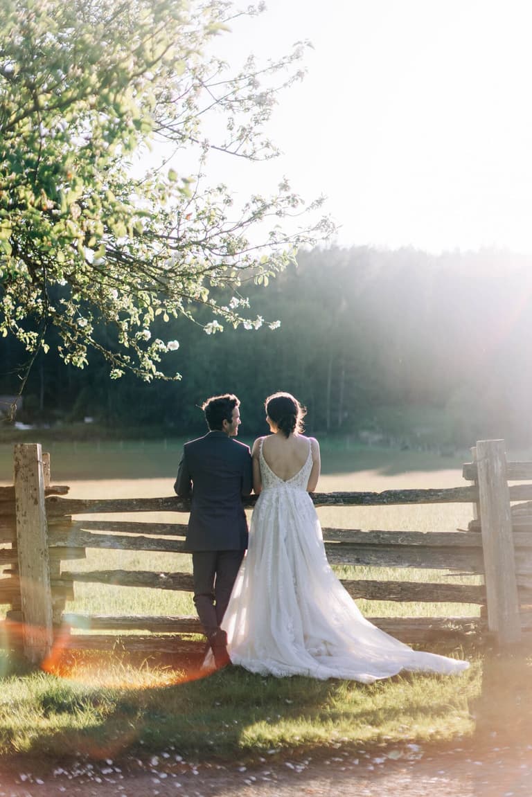 Bride and groom at a wooden gate beneath a blossoming tree