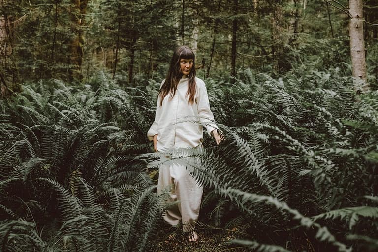 Woman in white walking through chest-high ferns, by Stasia Garraway
