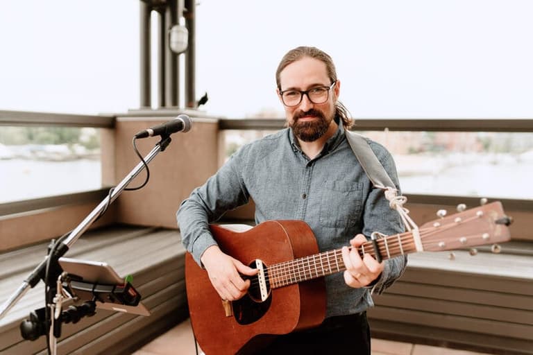 Noah Edwards playing acoustic guitar at a waterfront reception