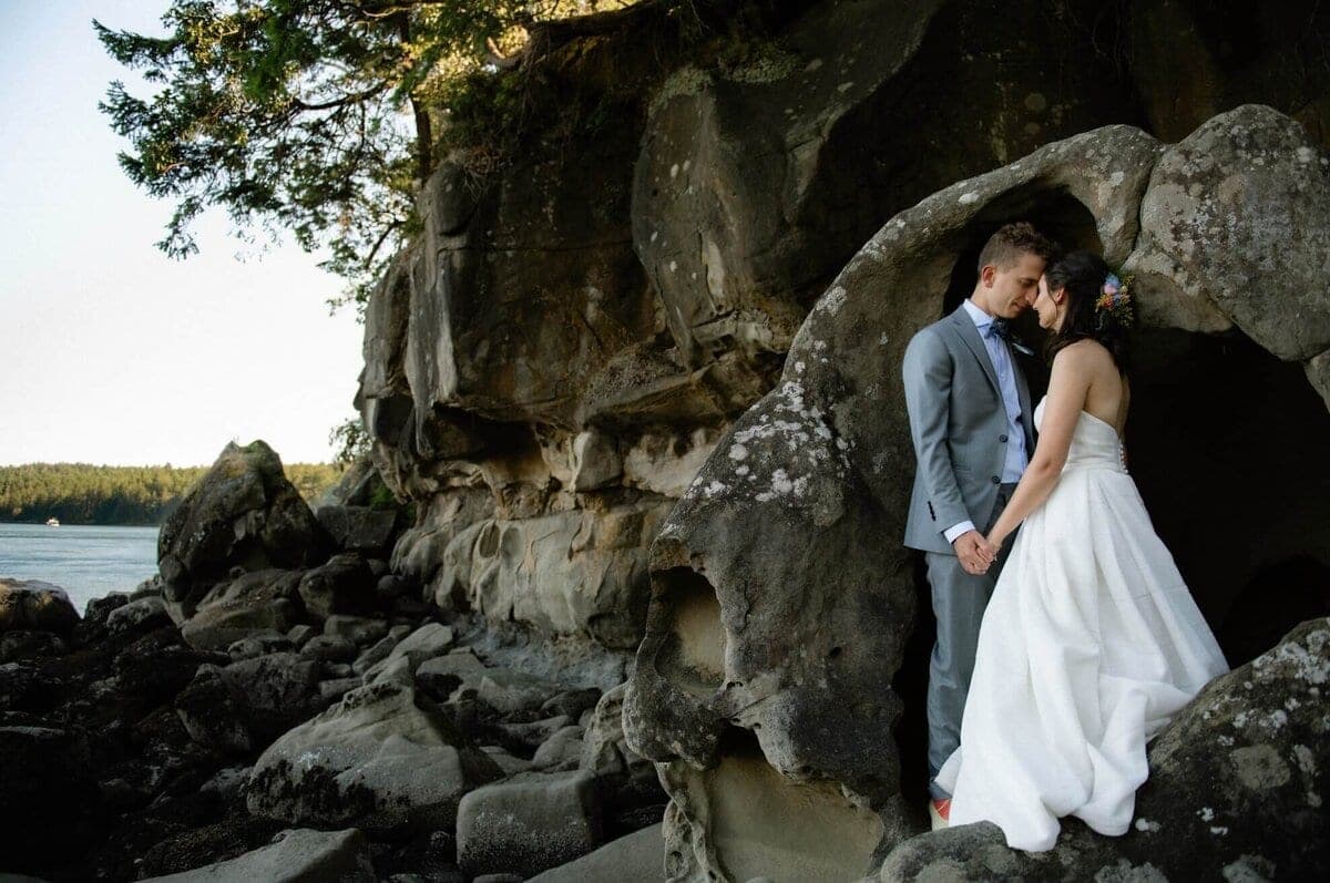 Newlyweds sheltered under a sandstone sea cliff at sunset
