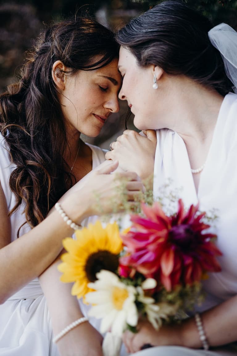 Brides touching foreheads over a sunflower and dahlia bouquet