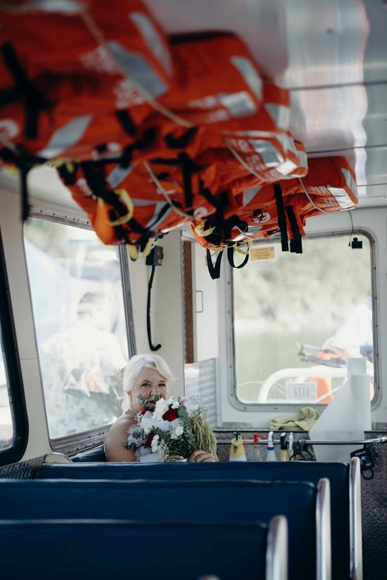 White-haired bride holding her bouquet inside a ferry cabin
