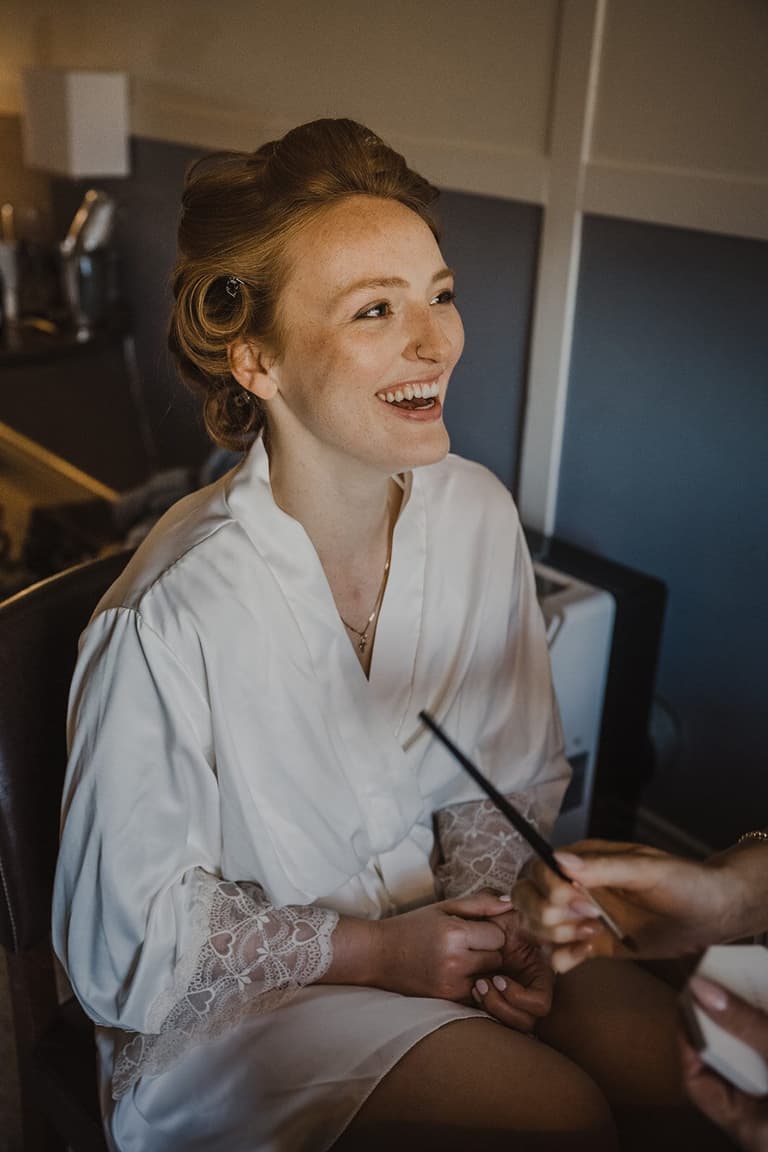 Laughing bride in a lace-trimmed robe during makeup preparations
