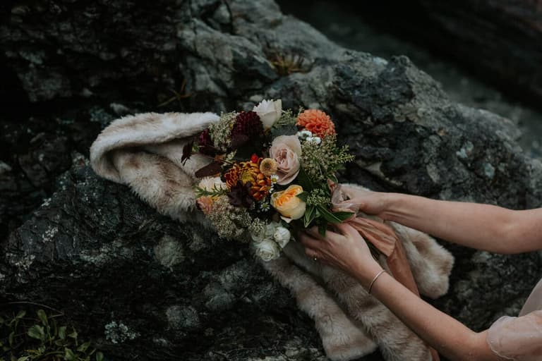 Hands settling an autumn-toned bouquet onto a fur wrap on rocks