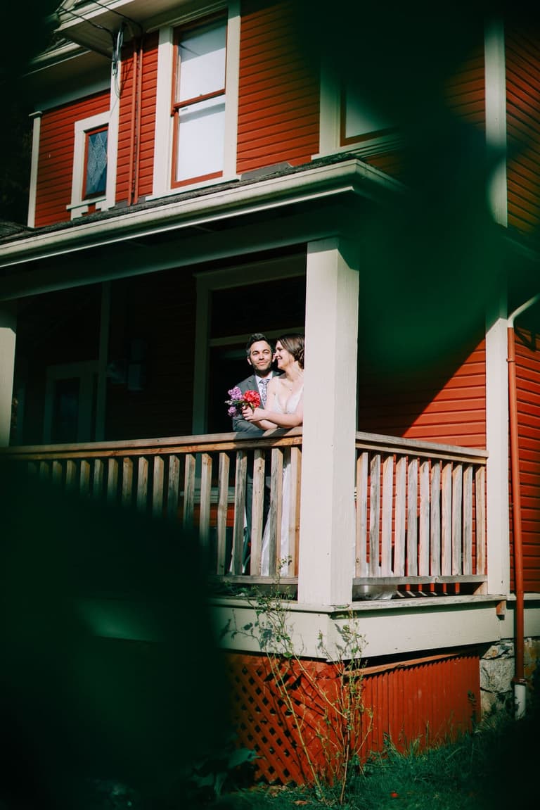 Newlyweds on the covered porch of the red farmhouse