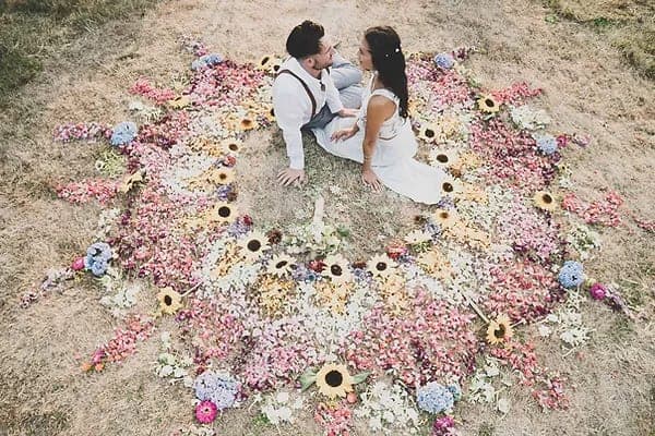 Couple in wedding attire embracing in center of circular floral arrangement with pink roses, sunflowers, and blue hydrangeas on grass at their Salt Spring Island wedding