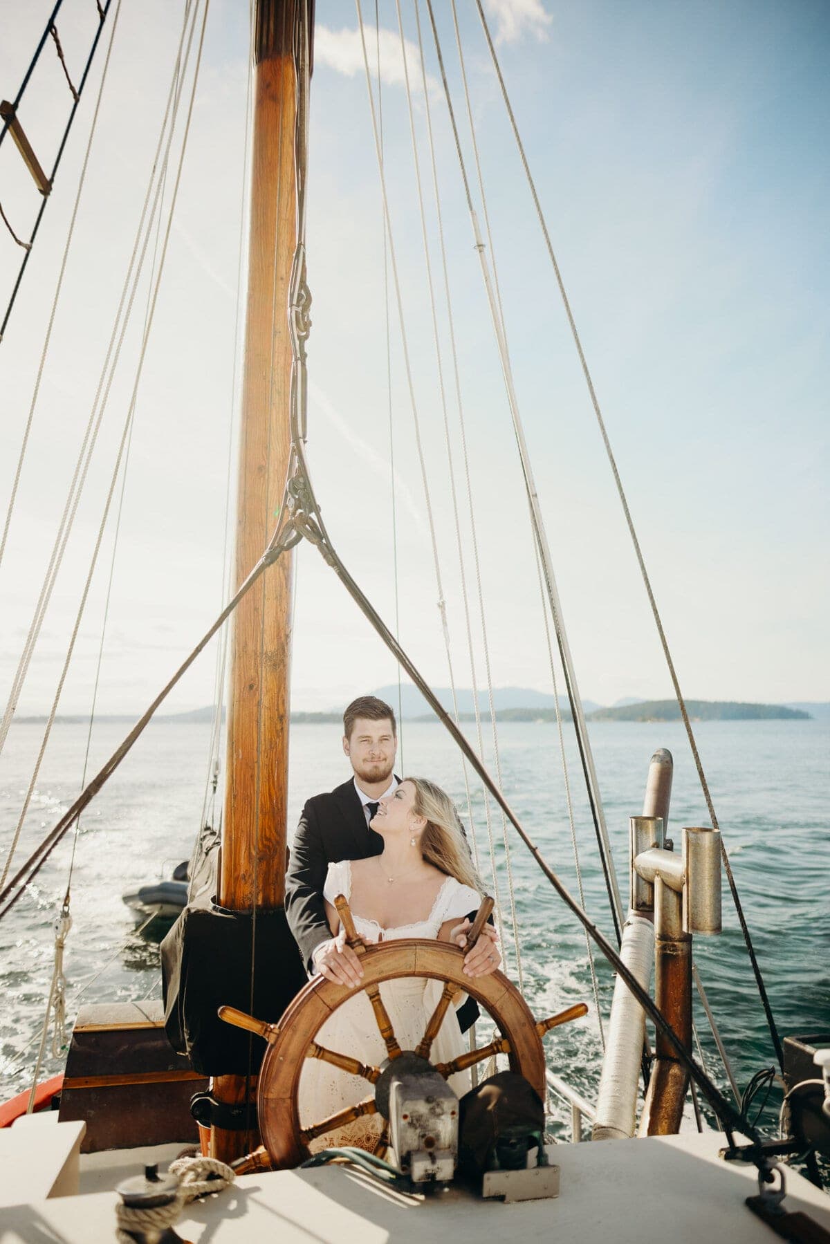 Groom at a sailboat's wheel, bride leaning against him