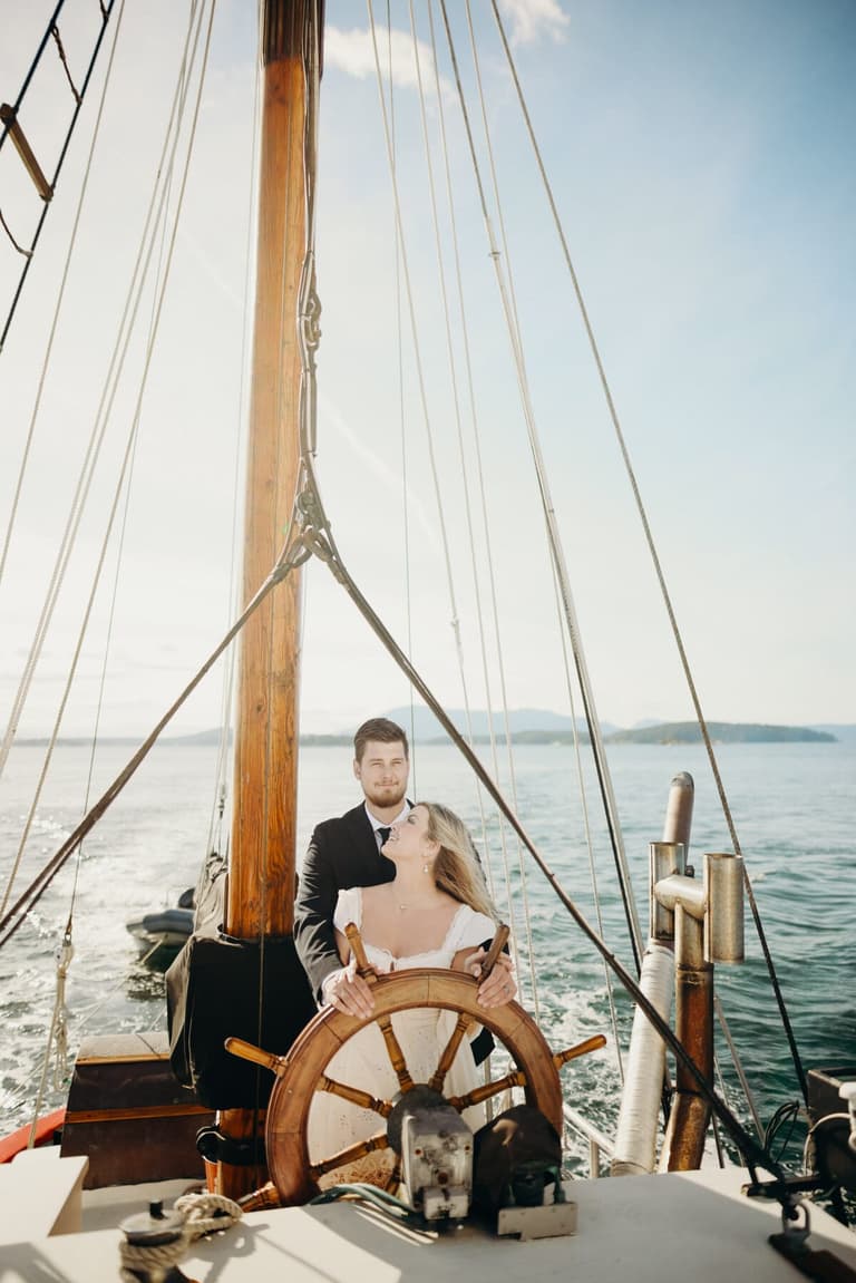 Newlyweds at the ship's wheel of a sailboat, dog beside them