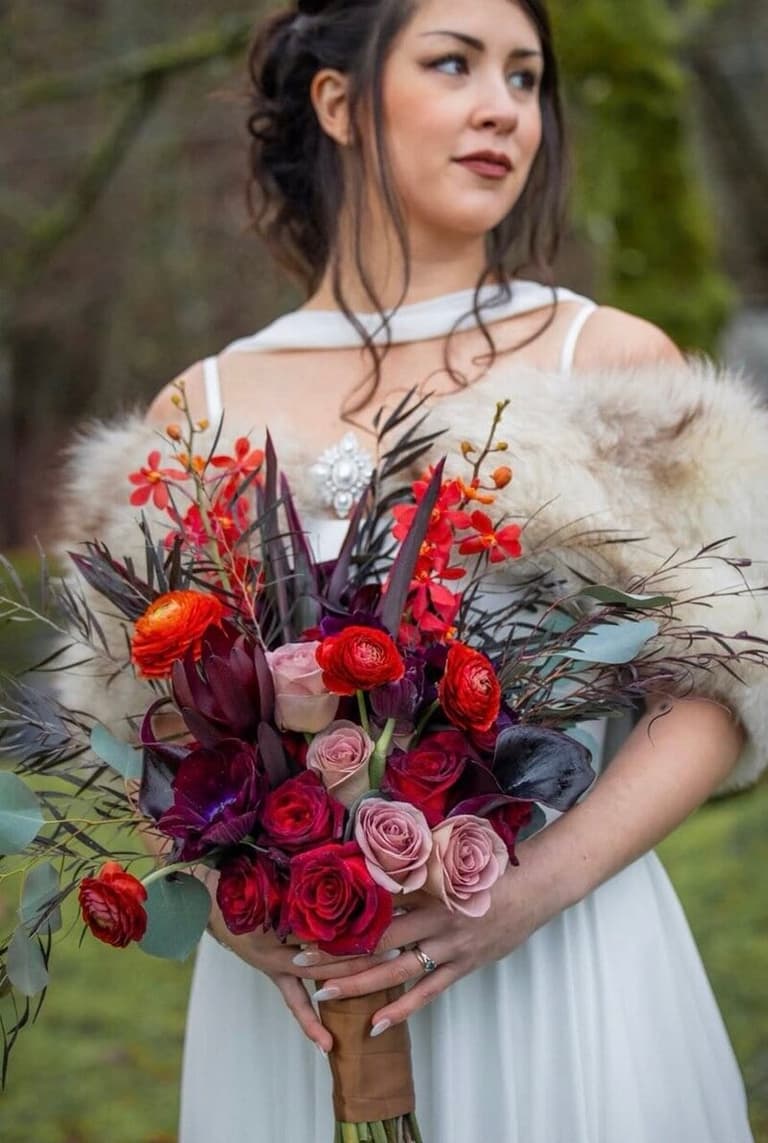 Bride in fur shawl holding a crimson rose bouquet by The Flower Guys