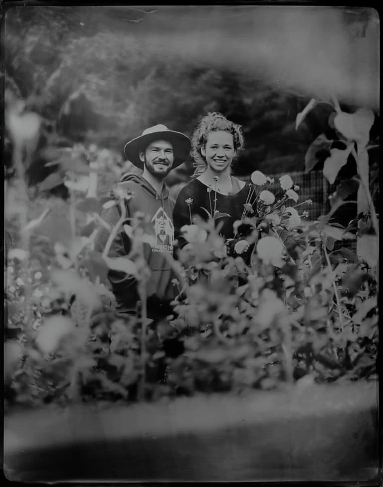 Smiling pair peeking through tall garden blooms, wet-plate style