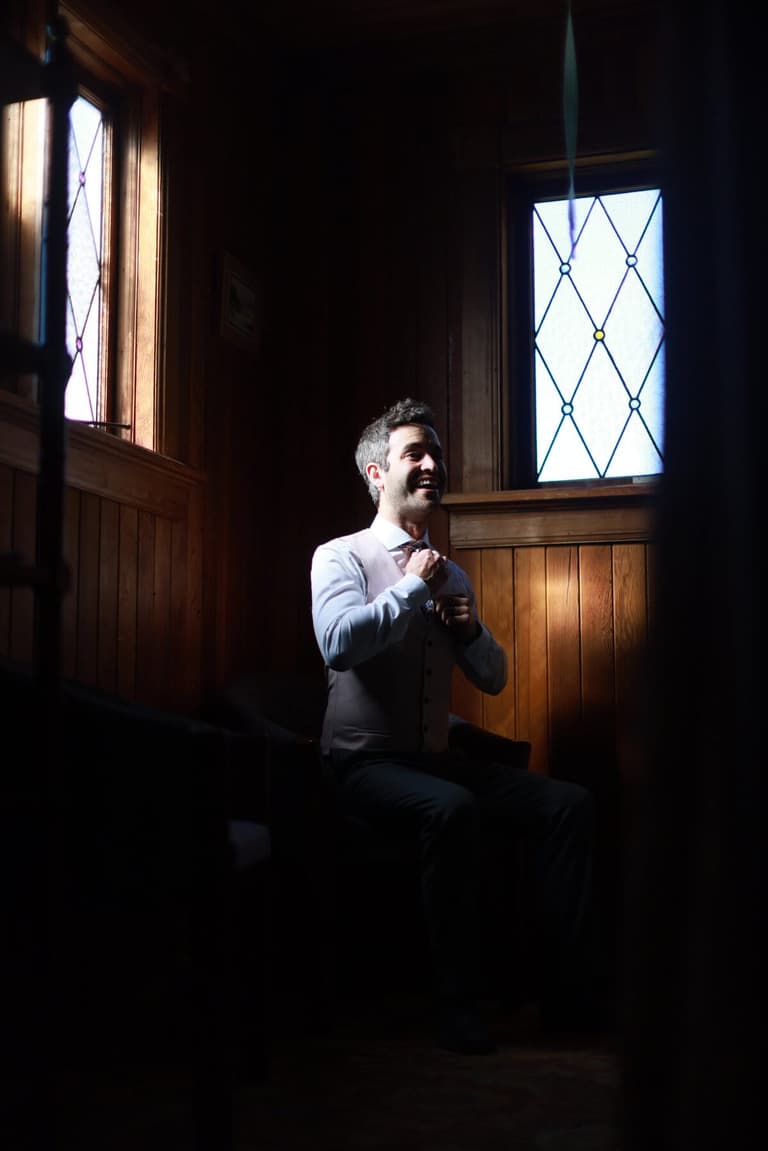 Groom buttoning his vest in a wood-panelled room