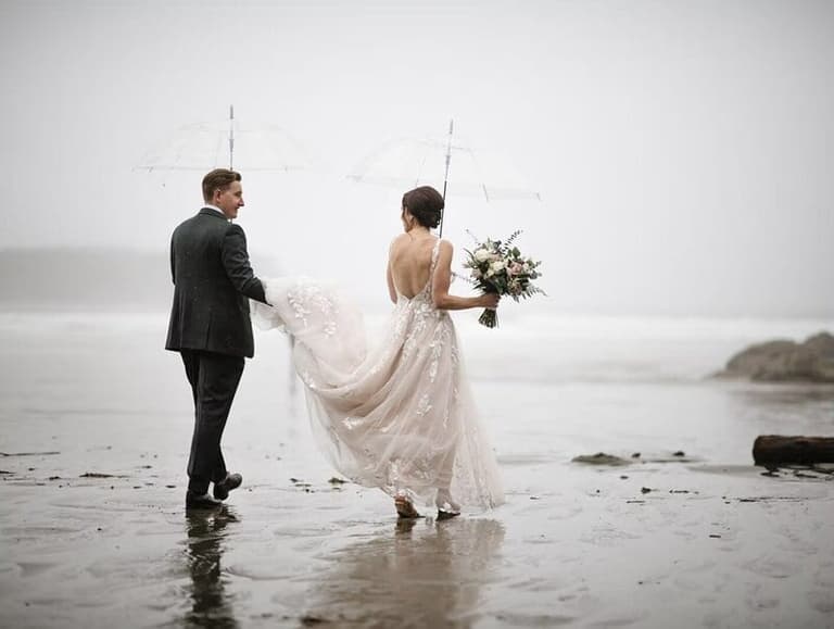 Newlyweds walk down beach in Tofino British Columbia on a rainy day