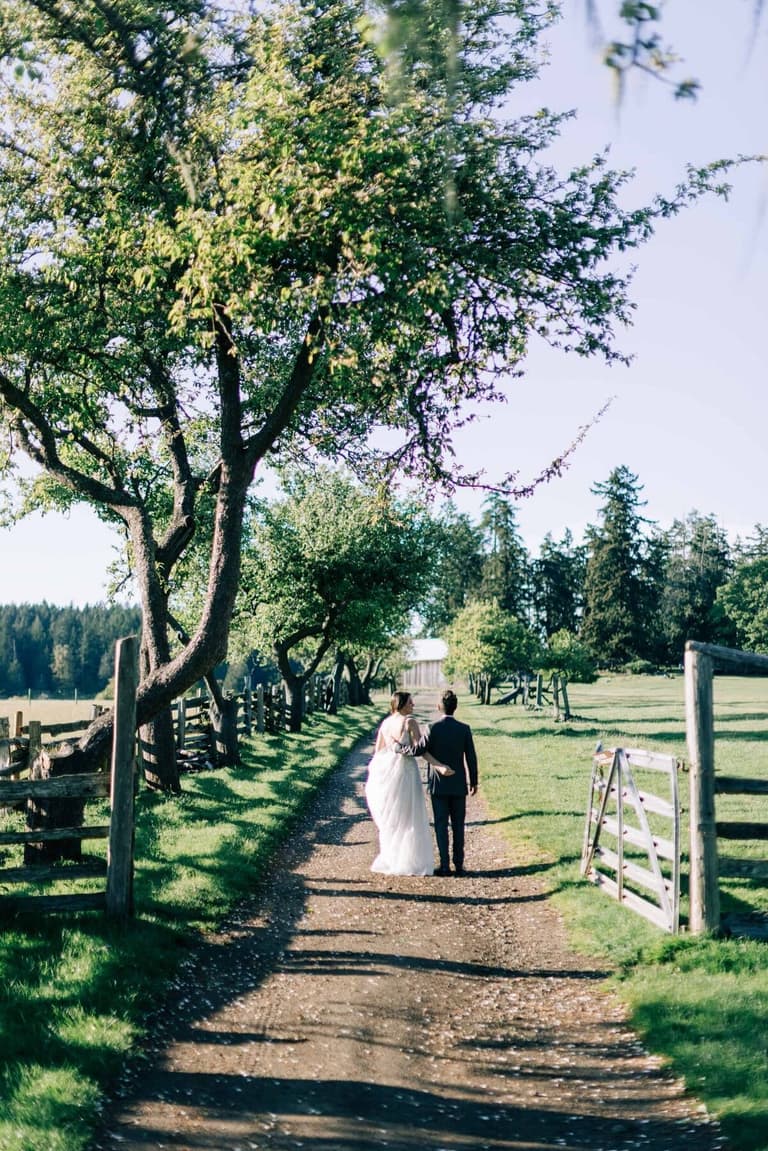 Couple strolling down a fenced dirt lane after the ceremony
