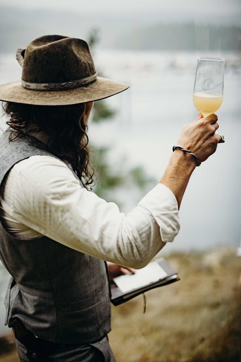 Long-haired officiant in a hat raising a toast above the harbour