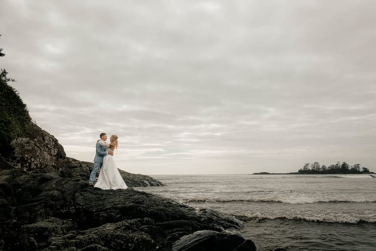 Couple standing together on ocean rocks with islands in the distance