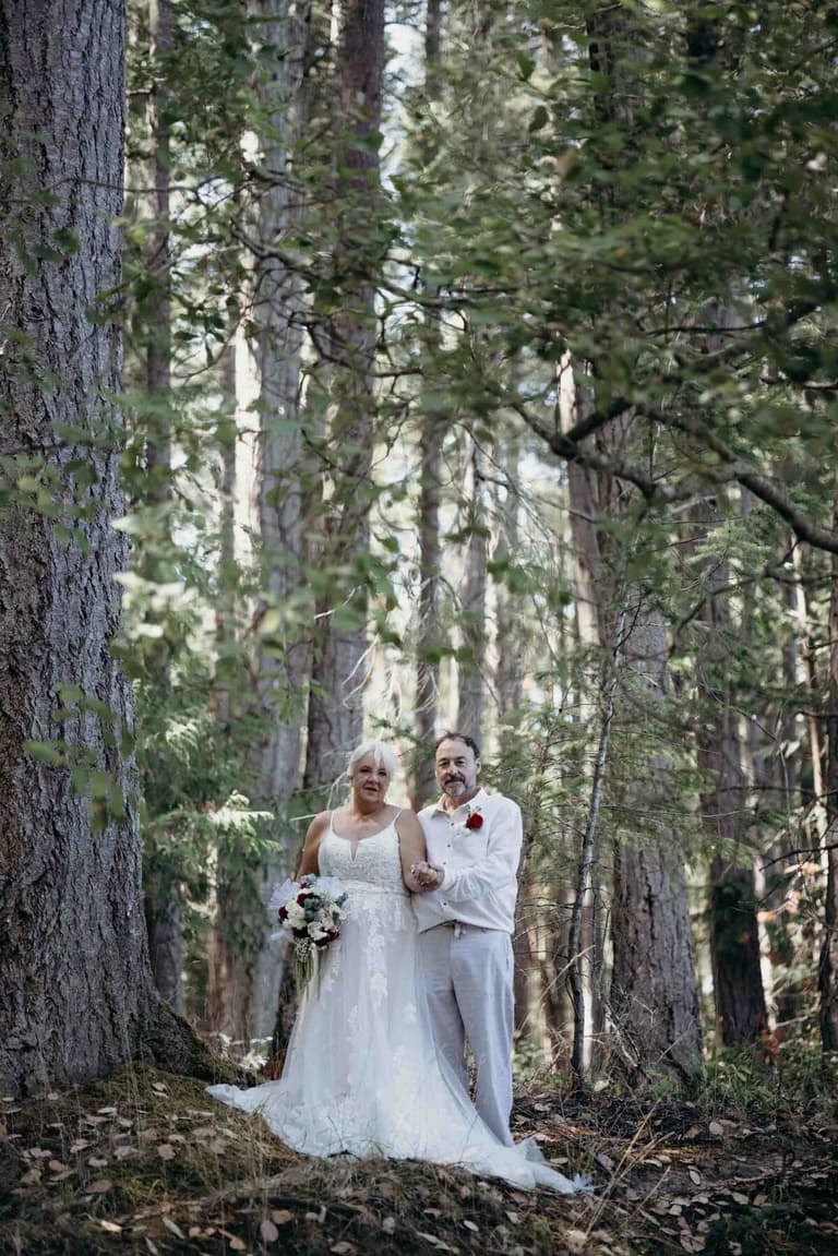 Older bride and groom dressed in white deep in the forest