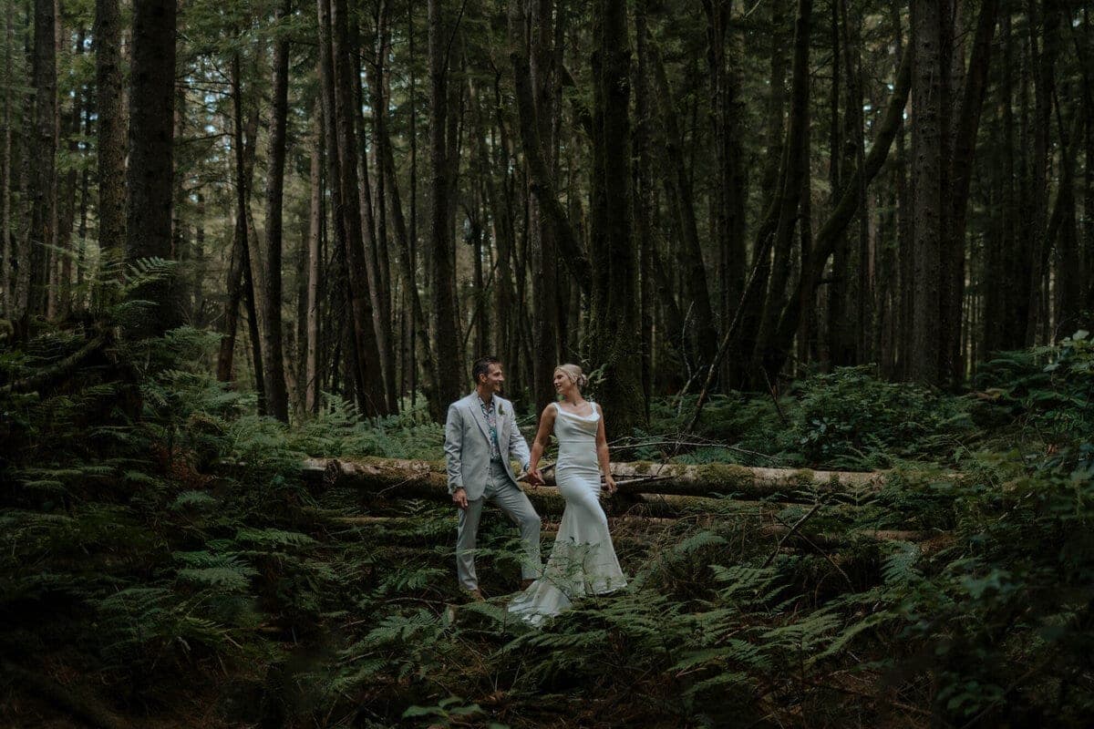 Eloping couple holding hands across a fallen forest log