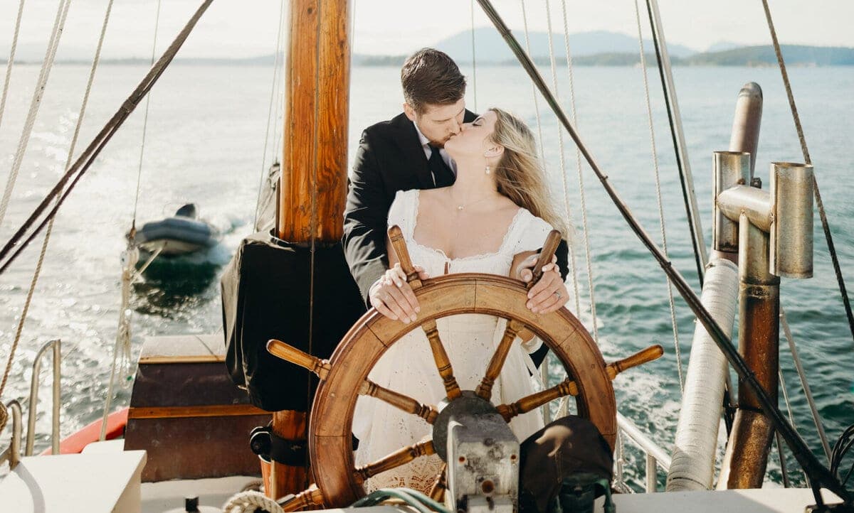 Couple kissing at the helm of a wooden sailboat
