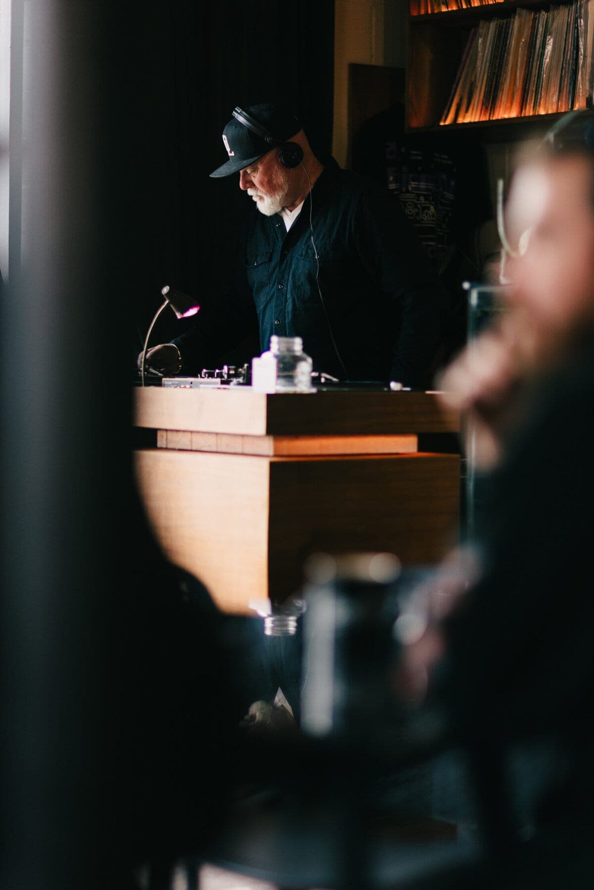 DJ behind a wooden booth with shelves of records behind him