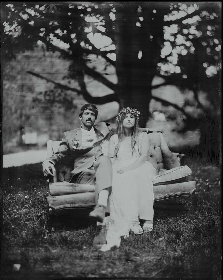 Flower-crowned bride and her groom lounging on an outdoor sofa