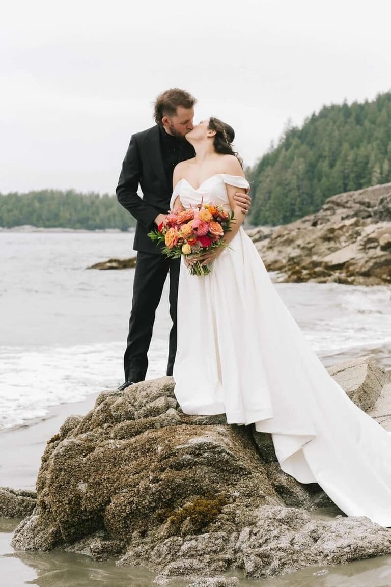 Bride's vivid coral bouquet by Fleur Tofino on a rocky shore
