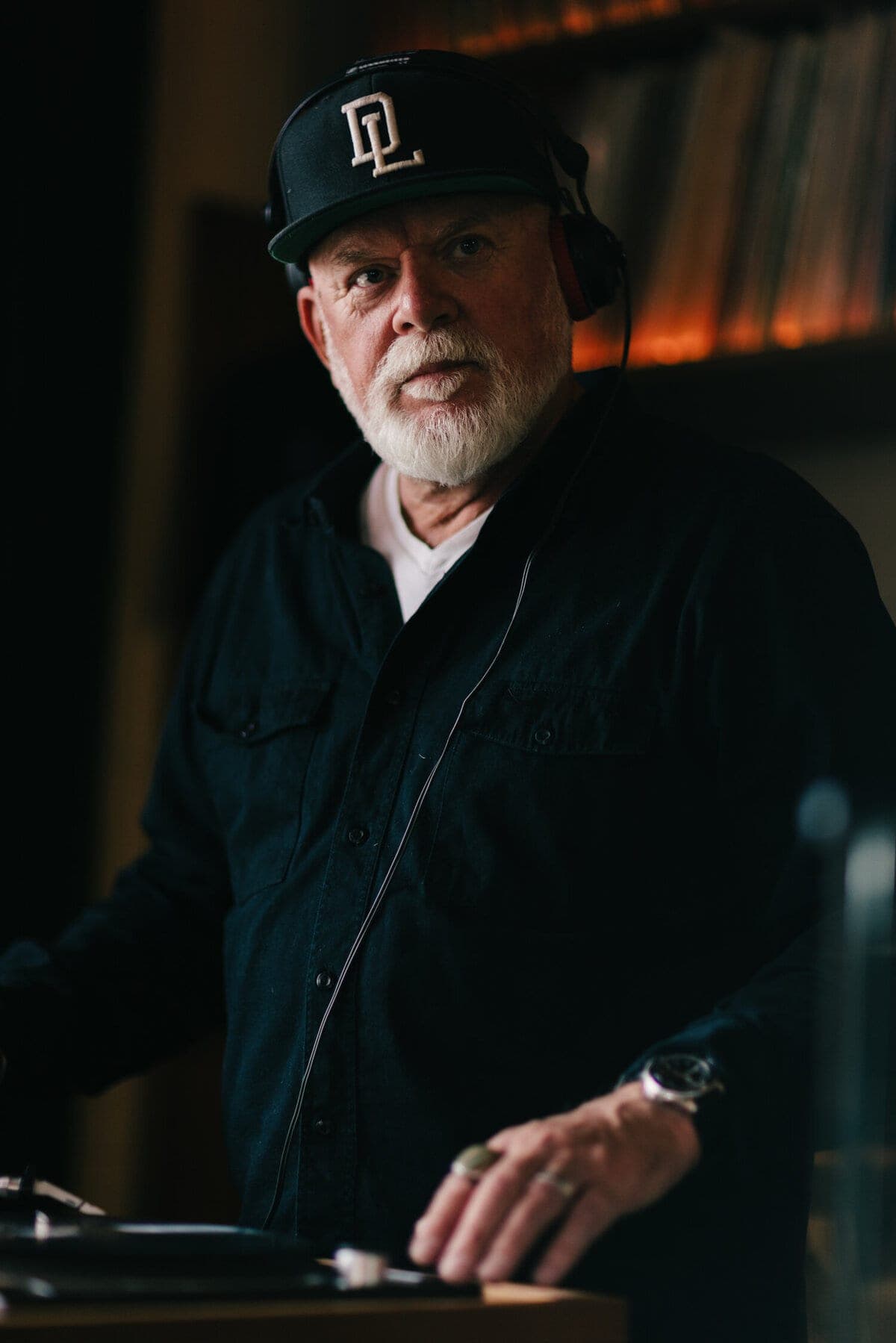White-bearded DJ in a ball cap glancing up from his turntable
