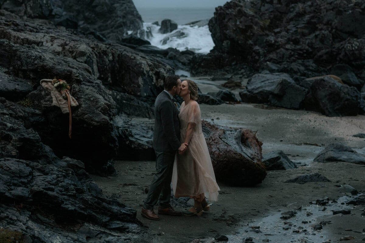Couple embracing among dark sea rocks on a stormy Tofino beach