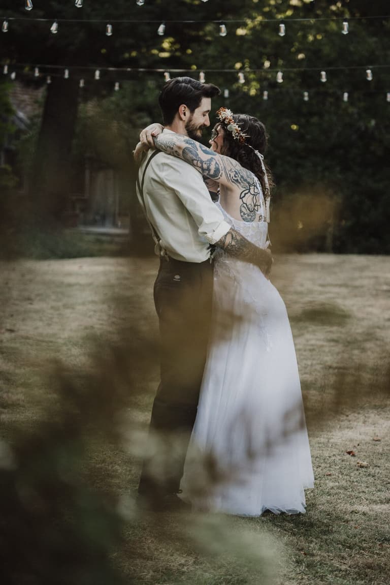 Tattooed couple sharing a first dance under string lights