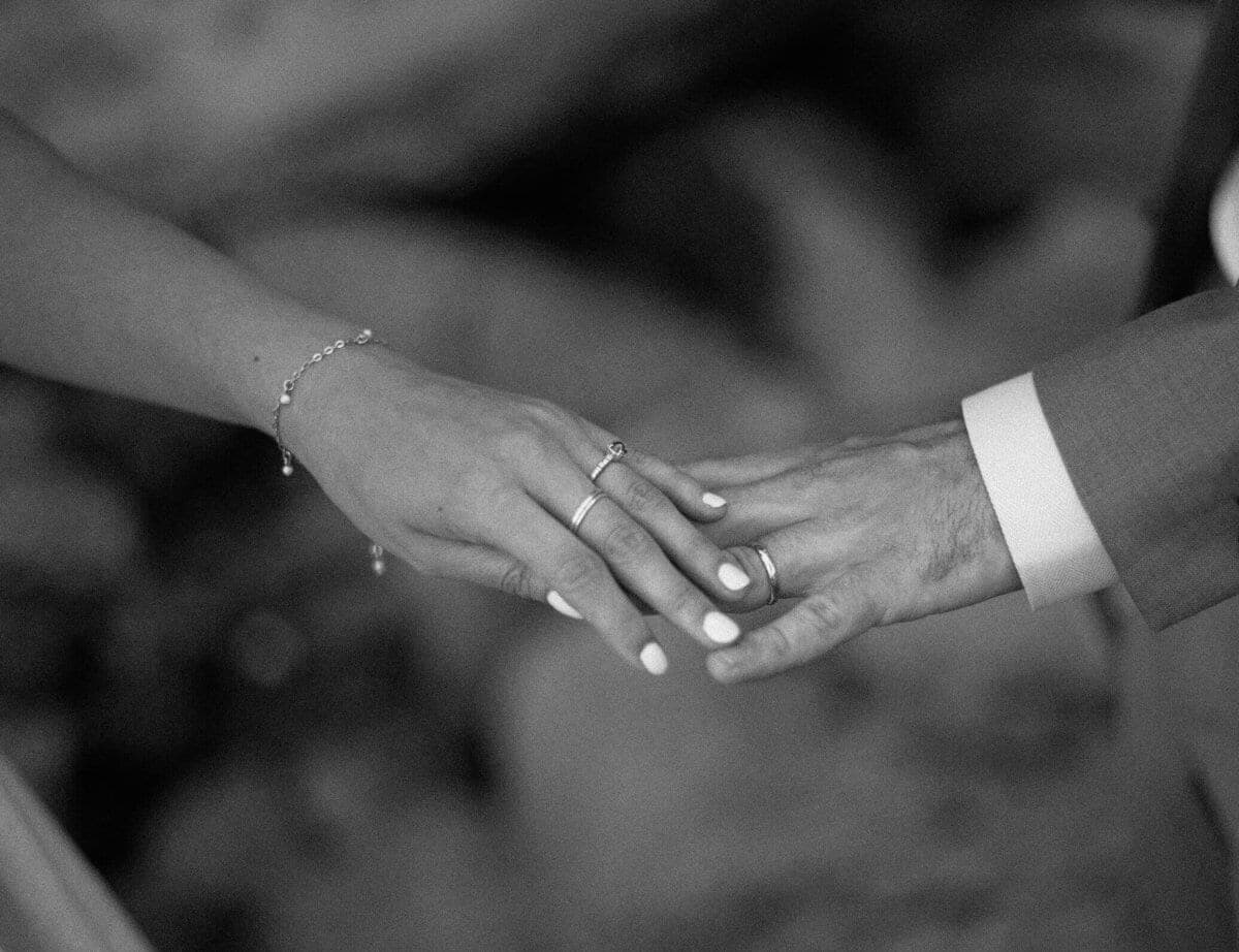 Close-up of two hands with white nail polish and silver rings resting together in black and white
